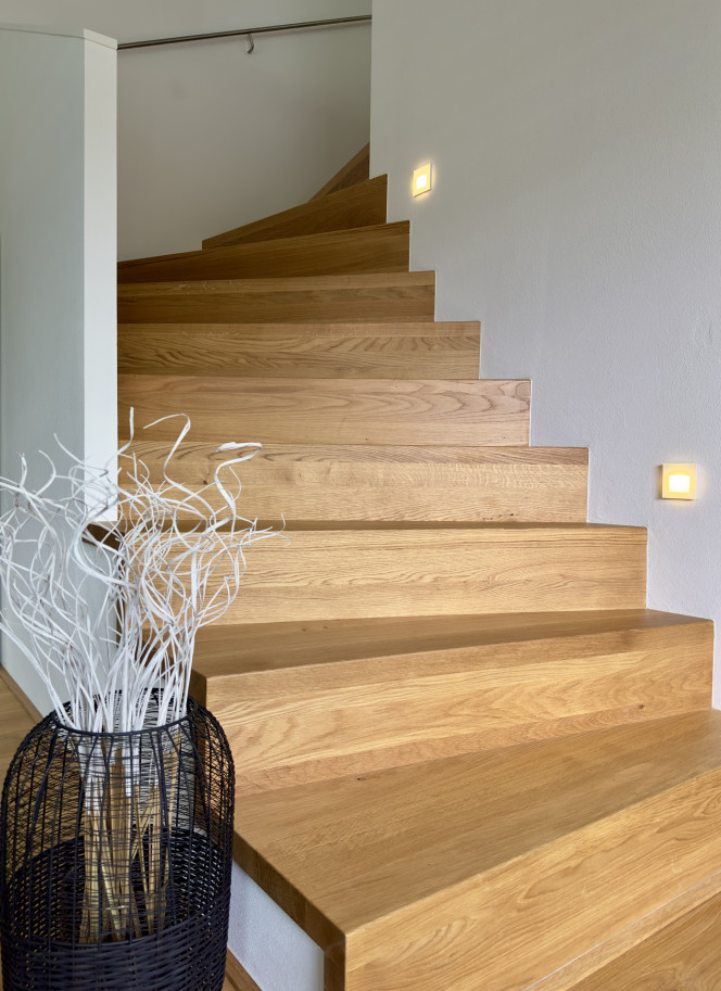Moderne Wangentreppe mit warmem Eichenholz und sanfter Lichtinszenierung entlang der Wand.
